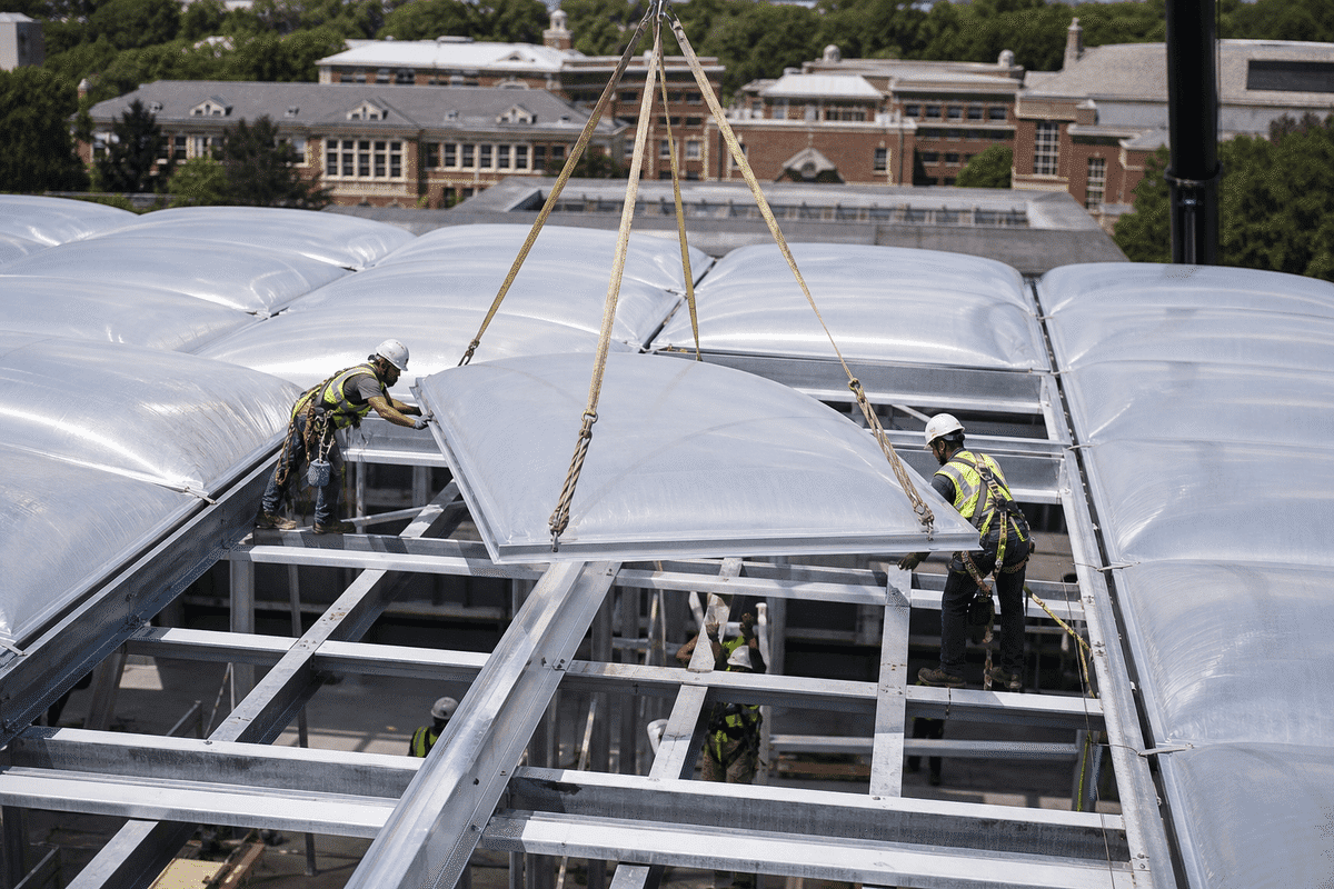 Construction crew installing ETFE cushion modules on a college roof grid