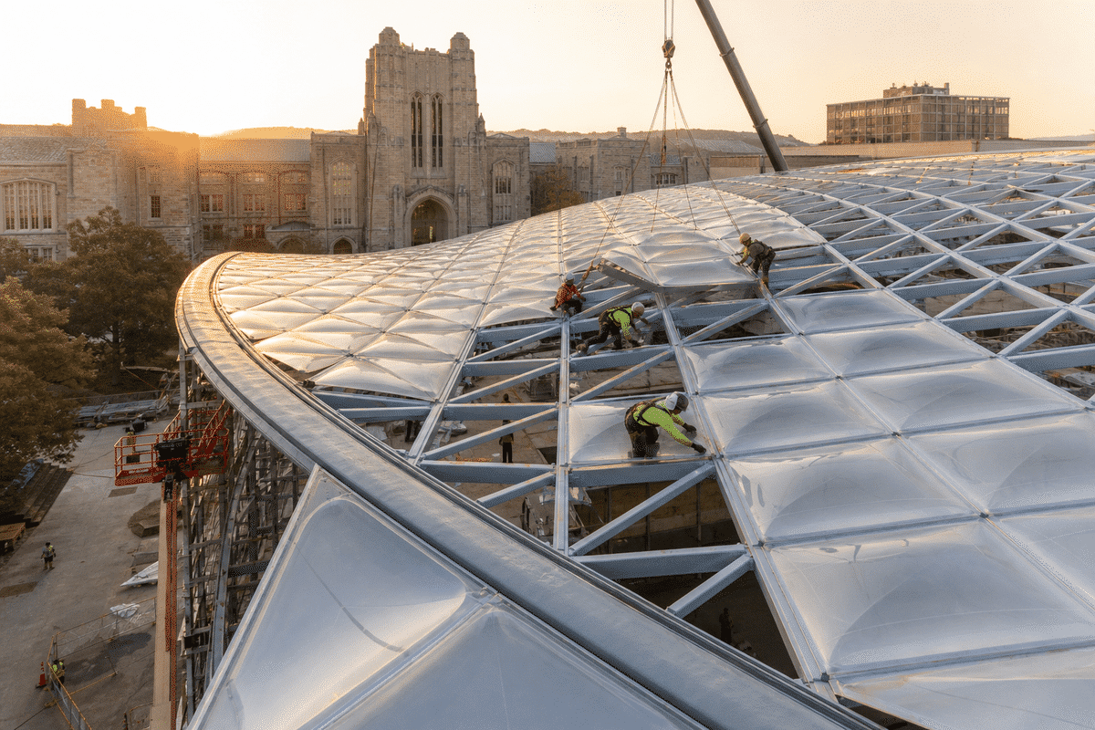 Construction crew installing ETFE cushion modules on a university roof grid