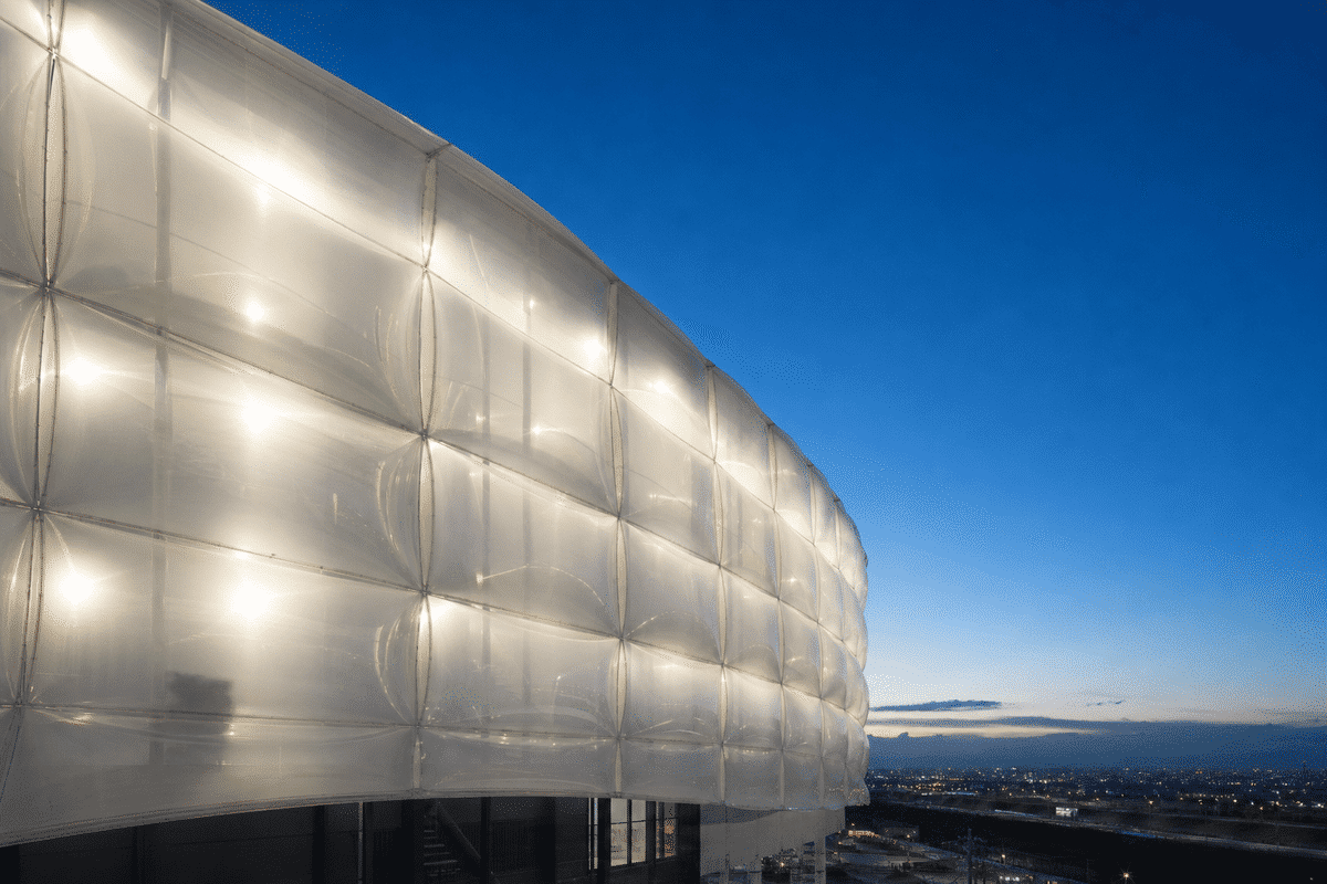 Translucent ETFE facade modules glowing under deep blue evening sky